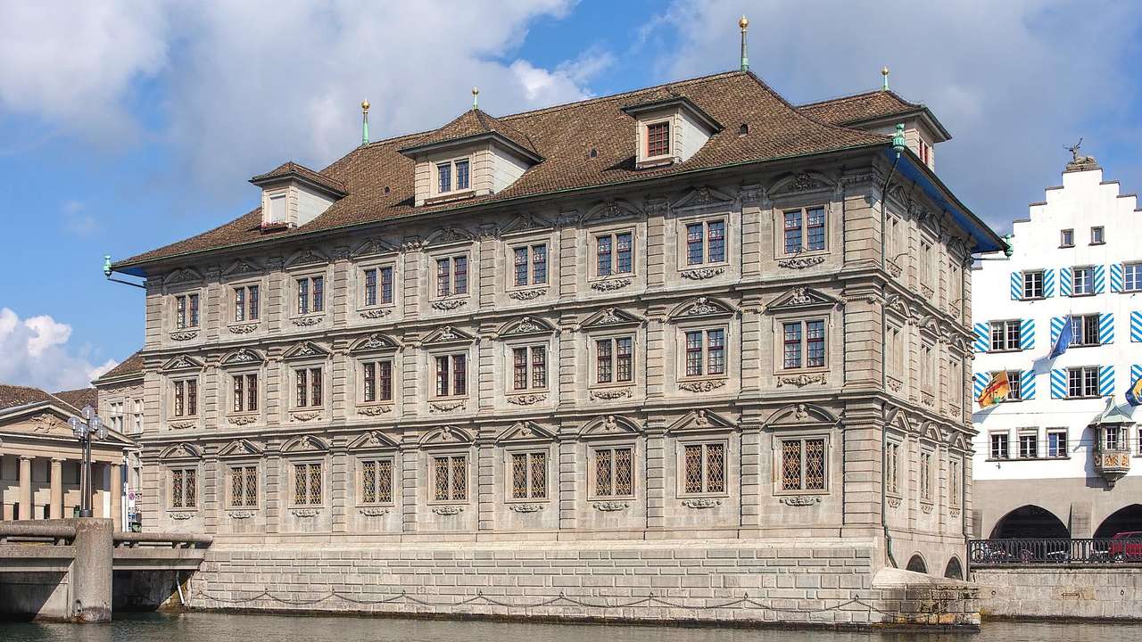 A Baroque and Renaissance gray building with a brown roof overlooking water