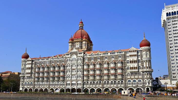 A palace with red domed roofs and a tall building beside it against a clear blue sky