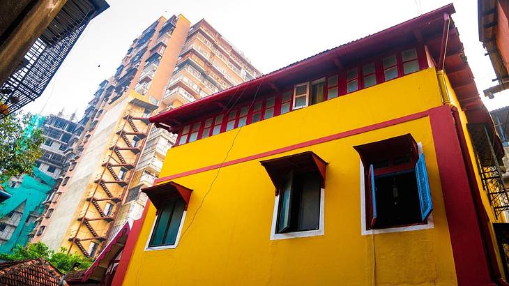 A yellow and red heritage house with a taller building beside it