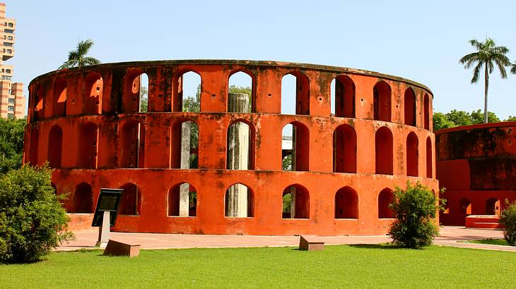 A round red structure with arched openings surrounded by green grass and a path