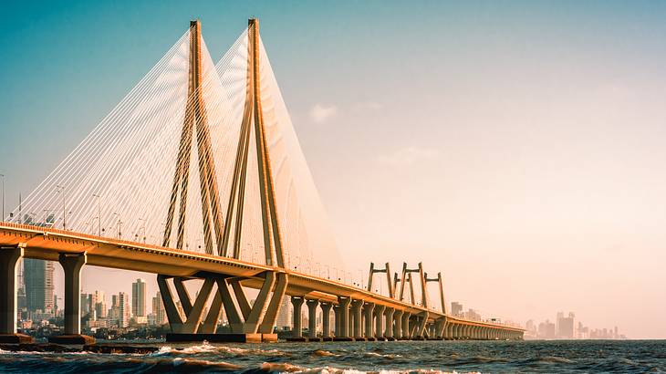 A large yellow steel bridge over the water with a city skyline in the distance