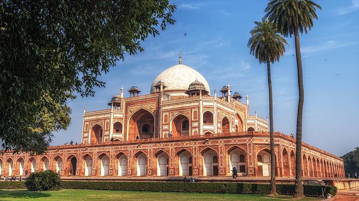 A white marble and red sandstone building surrounded by green grass and trees