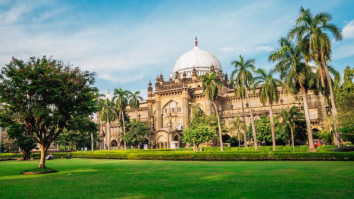 An old palace with a white dome with green grass and palm trees in front of it