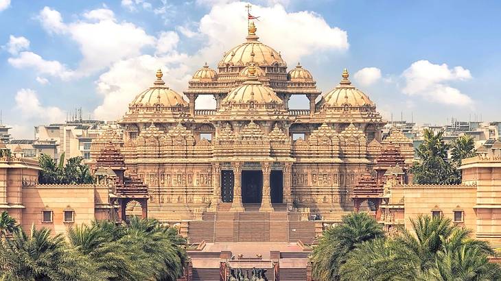 A staircase to a grand temple building with four domes under a partly cloudy sky