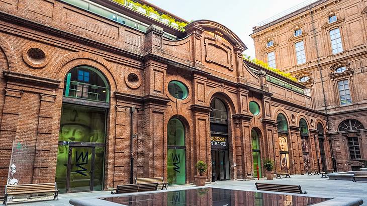 A brown brick museum building with arched glass doors and benches outside