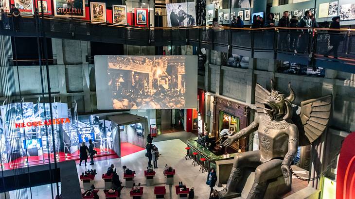 The interior of a museum with tourists watching a movie surrounded by exhibits