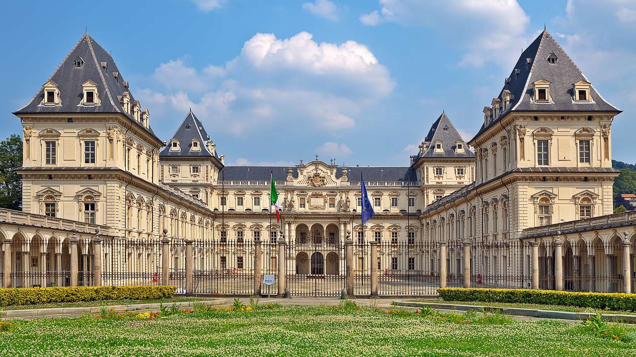 A cream coloured French Baroque-style mansion with a gray roof next to green grass