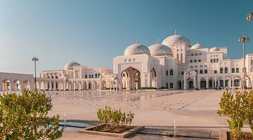 A white marble palace with arched columns and several domes under a clear sky