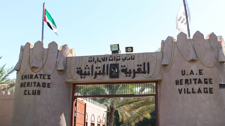 An old fort gate that says "UAE Heritage Village" with a UAE flag on top of it