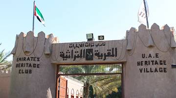 An old fort gate that says "UAE Heritage Village" with a UAE flag on top of it