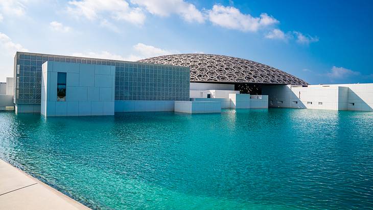 A contemporary white building with a round artistic gray roof next to a pool of water