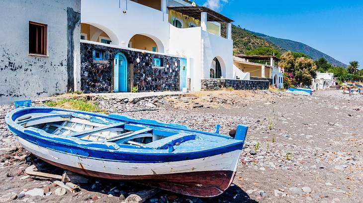 A blue and white wooden boat sitting on a sandy shore next to a white building