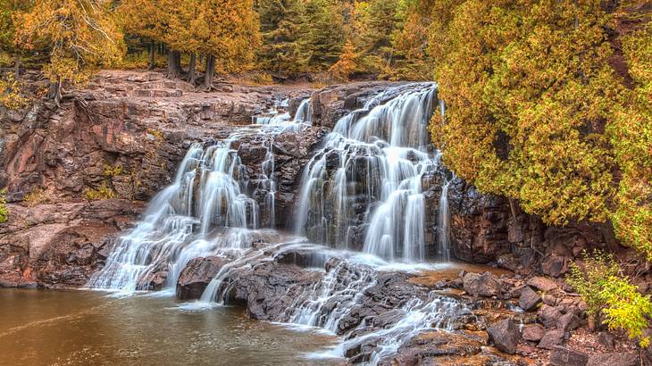 A cascading waterfall flowing down a rocky cliff surrounded by autumn trees A cascading waterfall flowing down a rocky cliff surrounded by autumn trees