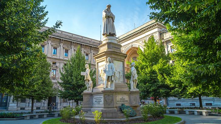 A bronze statue of a man next to a historical building surrounded by greenery