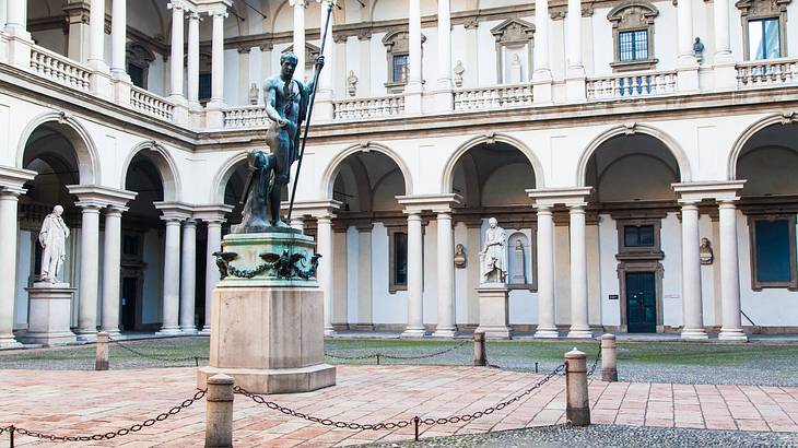 A statue of a man inside a courtyard with white arched columns surrounding it