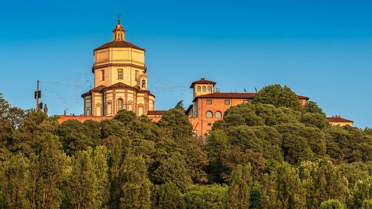 Green trees surrounding a Renaissance-style church building under a clear blue sky