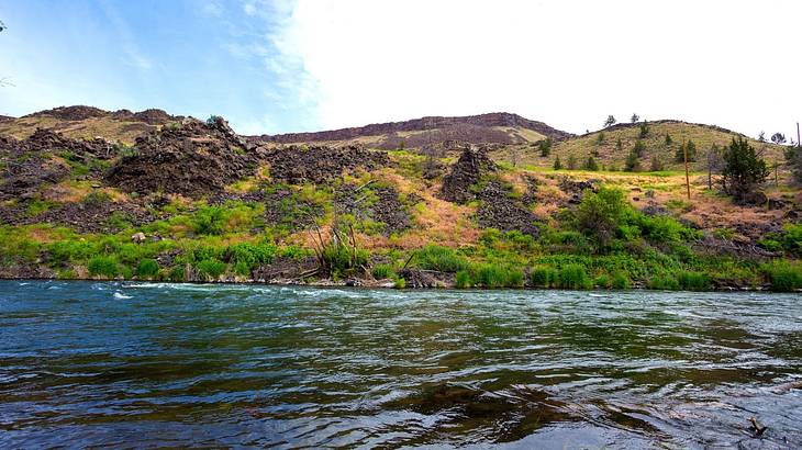 Green hills in the background with water in front on a partly cloudy day