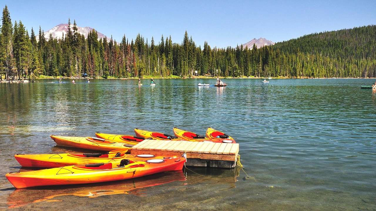 Multiple yellow kayaks moored in water, surrounded by evergreens and blue sky