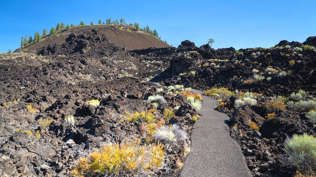A walkway between black volcanic rocks leading to a cinder cone at the far back