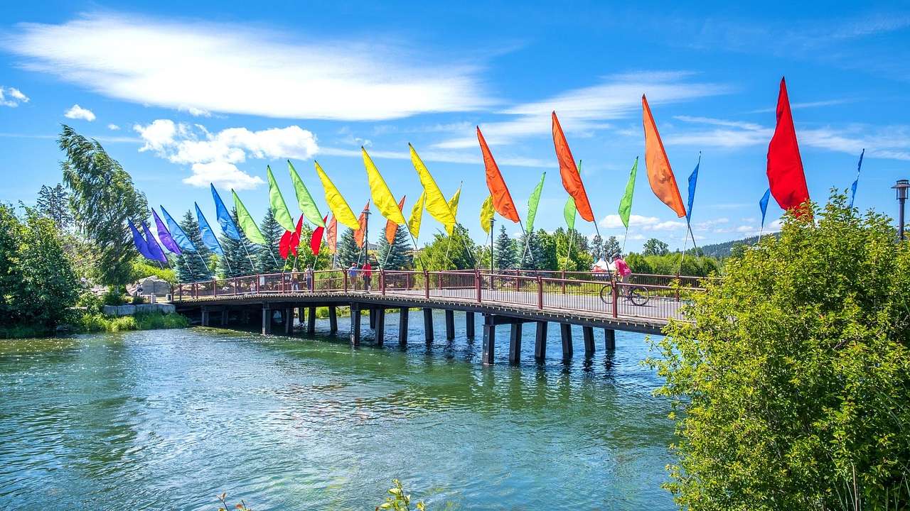 A bridge lined with multi-color flags over water under a partly cloudy sky