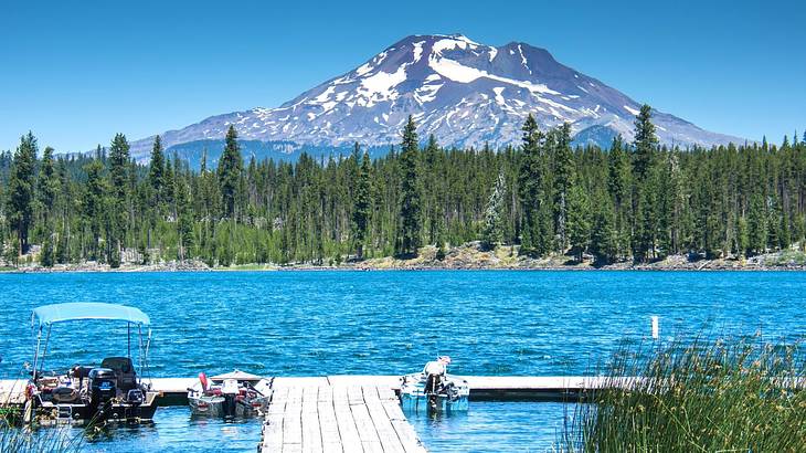 A dock on a blue lake against green pine trees and a snow-capped mountain
