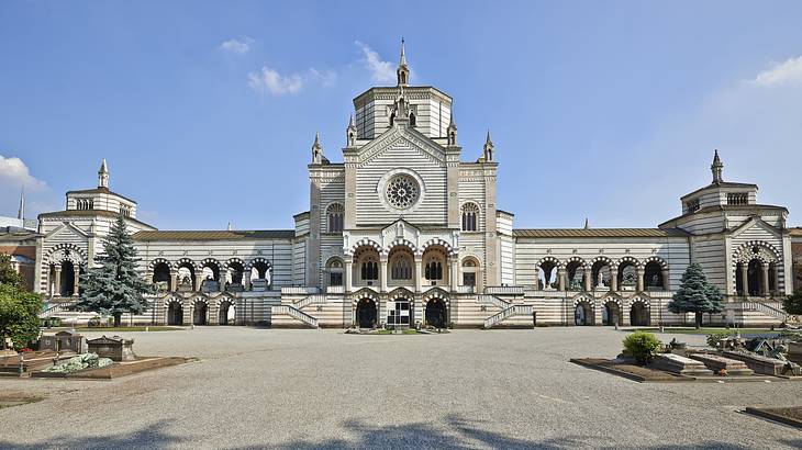 A white cemetery building with arched columns against a blue sky with some clouds