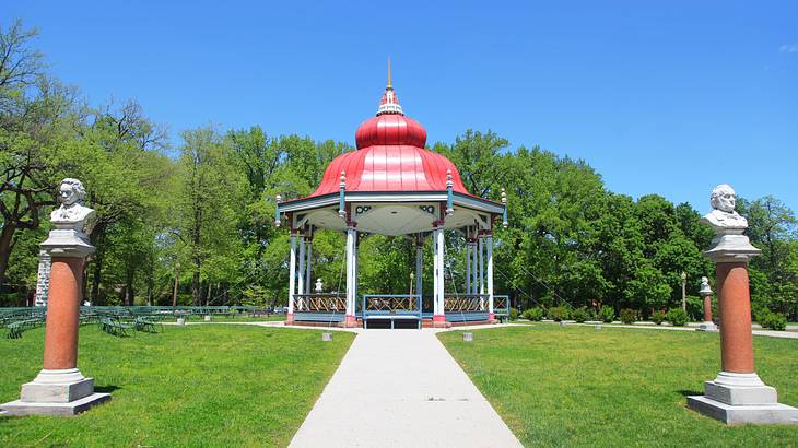 A walkway through the grass to a gazebo with a red roof and green trees behind it