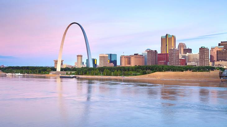 A skyline and a huge arch monument next to a river under a purple sky