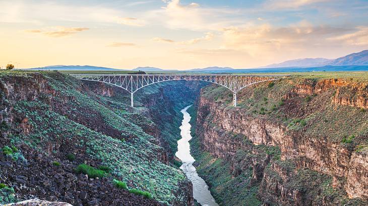A steel deck arch bridge over a gorge covered with greenery under a partly cloudy sky