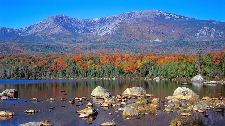 A mountain with autumn trees and a lake with boulders in front of it