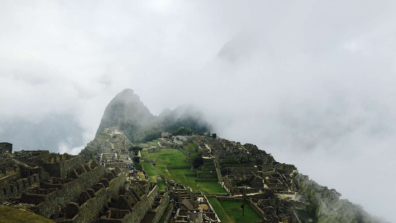 Ancient Inca ruins on a green mountaintop, surrounded by clouds from above