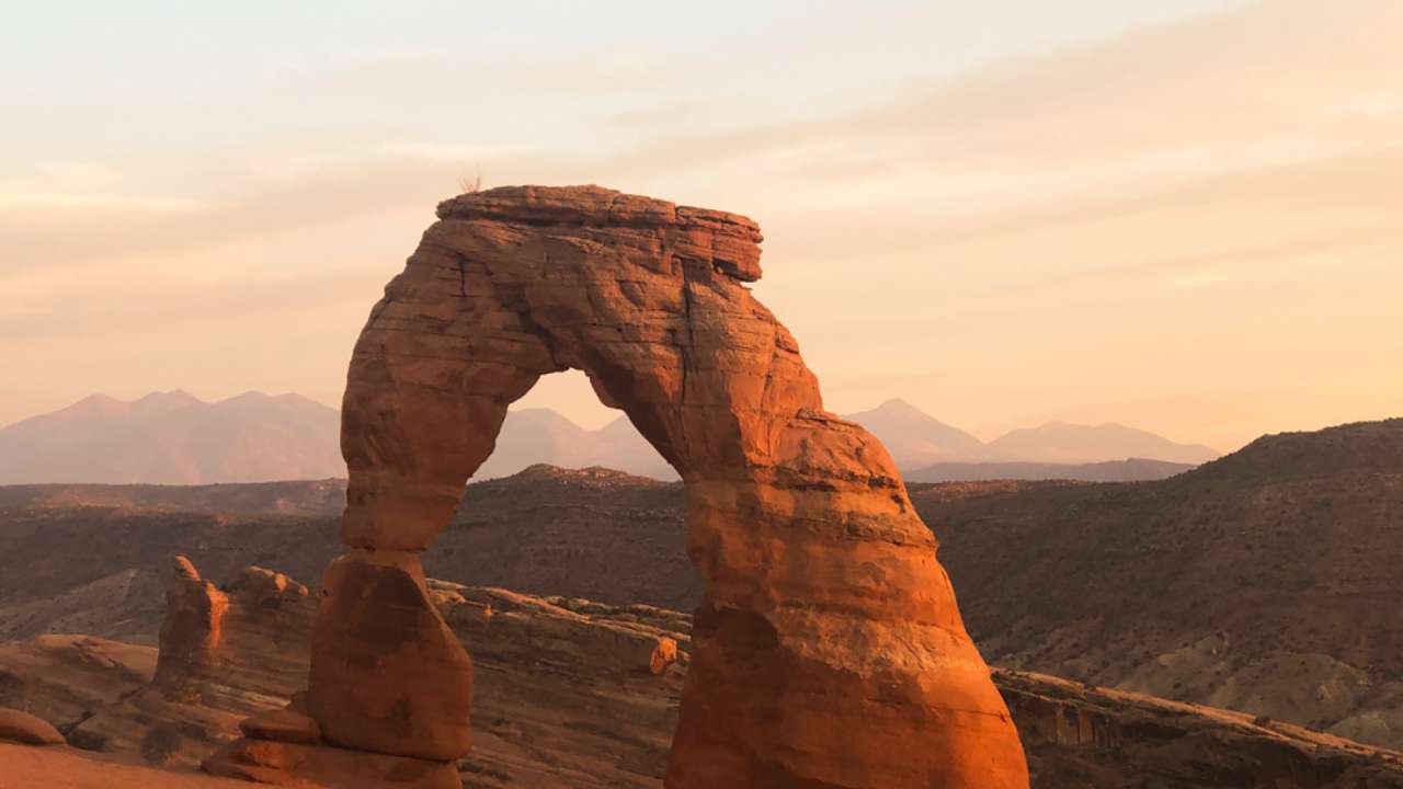 A uniquely-shaped sandstone arch surrounded by canyons at sunset