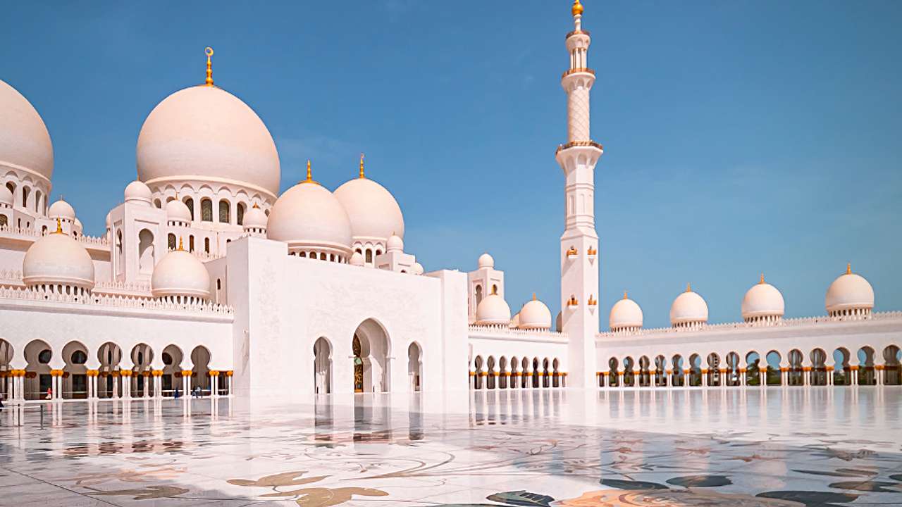A grand white mosque with a pinkish glow against a blue sky