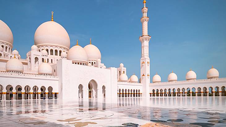 A grand white mosque with a pinkish glow against a blue sky