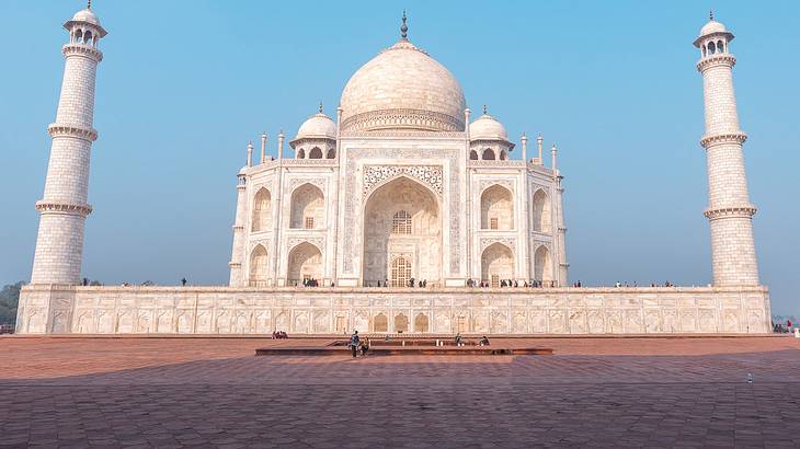 The grand white Taj Mahal with two tall towers on either side, on a blue day