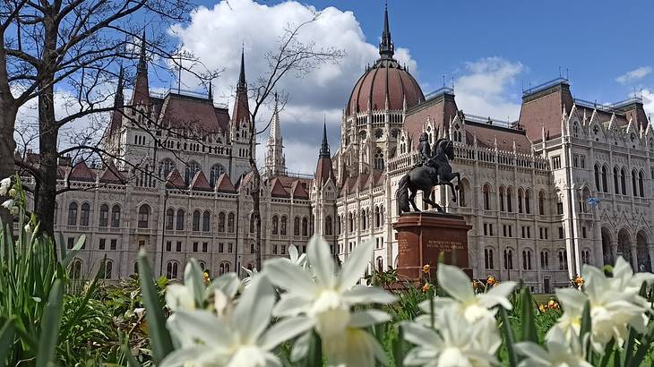A massive parliament building with a statue and white flowers in front