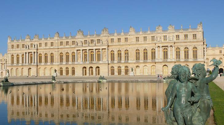 A massive palace with water and a statue in front against a blue sky
