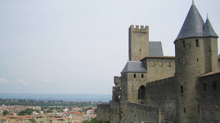 A grey castle with walls on a hill overlooking a historic city