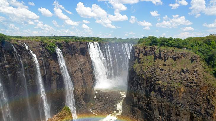 A rainbow near waterfalls rushing down green-covered rocky cliffs