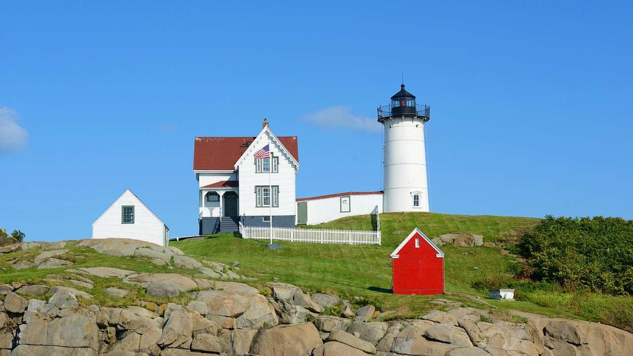 A lighthouse with a black top next to a small white house on a grassy hill