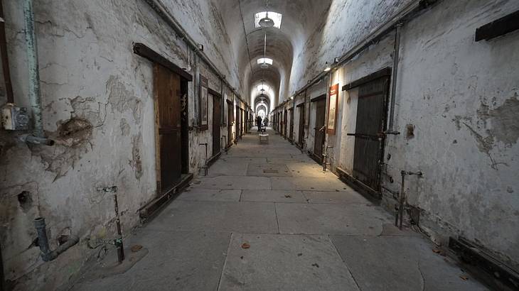 The inside of an old and abandoned prison with white stone walls and wooden doors