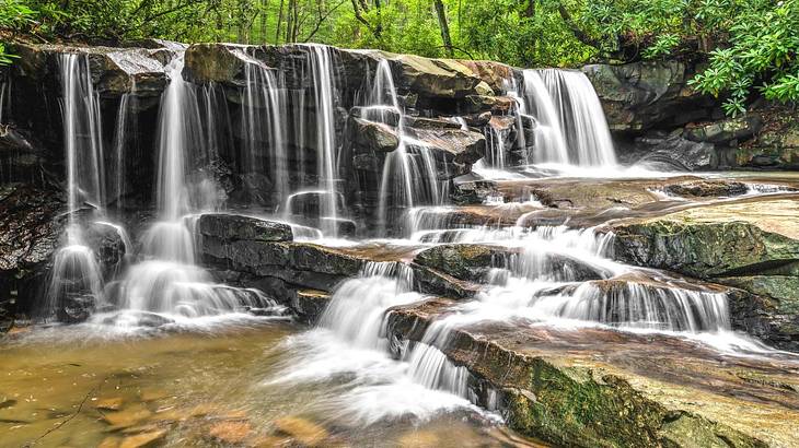 A waterfall with many streams of water flowing into a river surrounded by greenery A waterfall with many streams of water flowing into a river surrounded by greenery