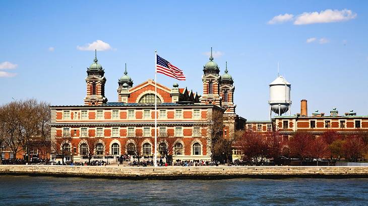 A red brick building on an island with a US flag and water in front of it