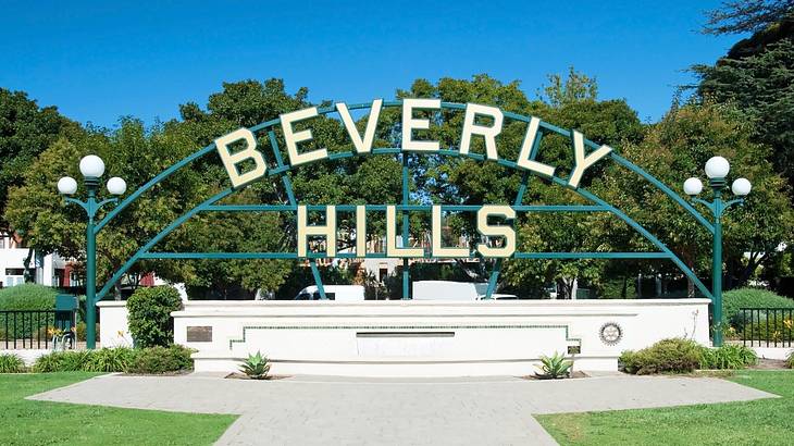 A sign that says "Beverly Hills" with a lawn, trees, and a path around it