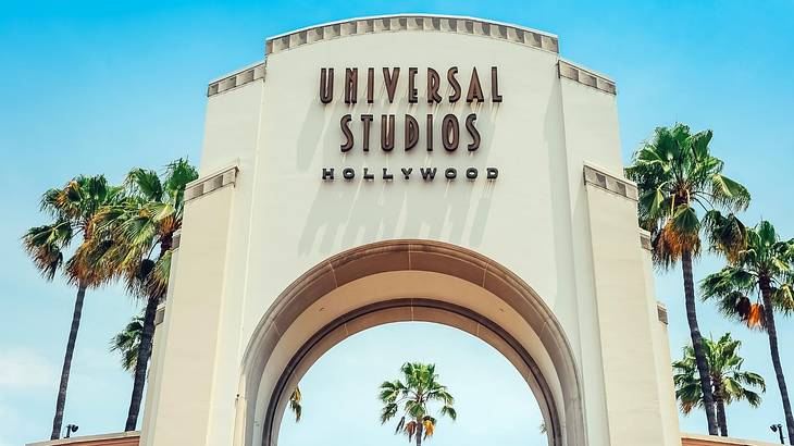 A white arch with a "Universal Studios Hollywood" sign and palm trees next to it A white arch with a "Universal Studios Hollywood" sign and palm trees next to it