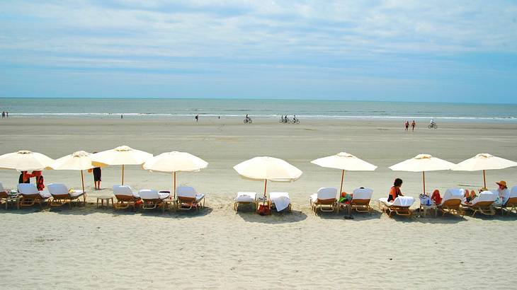 A beach with people on sunbeds under sun umbrellas