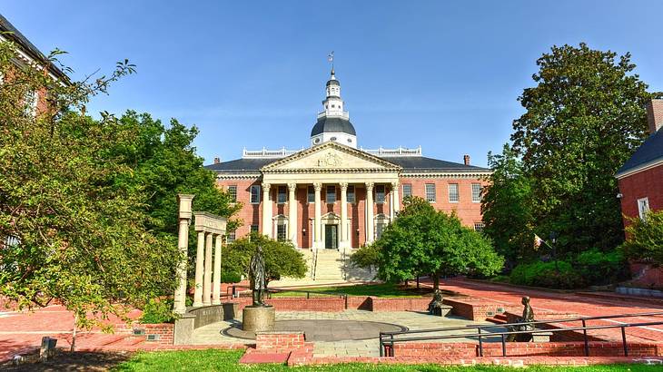 A neoclassical capitol building with white columns and a gray roof behind a courtyard