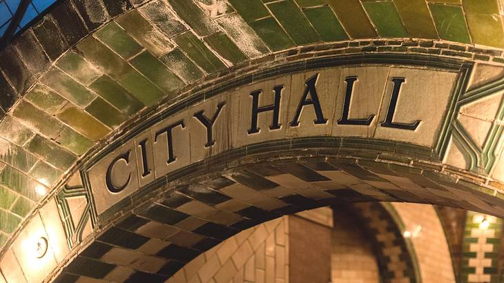 A close-up of an archway covered in tiles with a sign that says "City Hall"