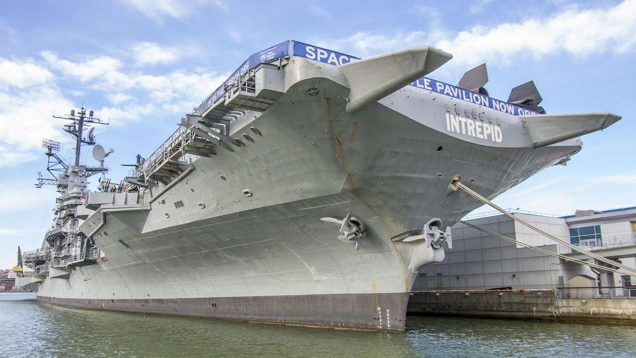 A grey aircraft carrier in the water with the words "Intrepid" painted on it