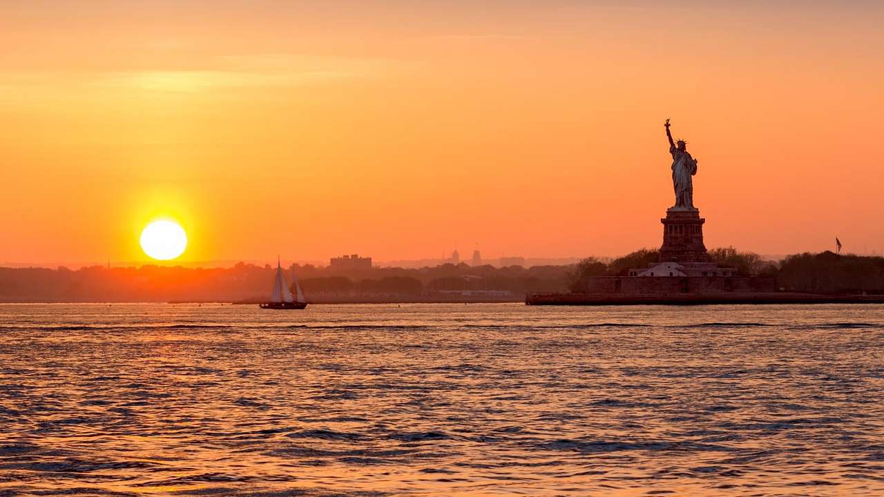 Water with boats on it and the Statue of Liberty on the right-hand side at sunset